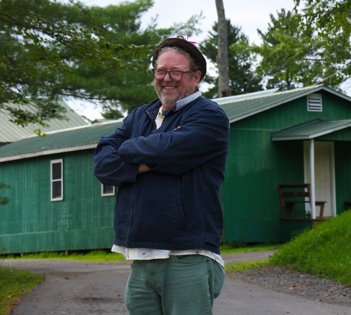 Dr. Lewis smiling in front of a cabin at band camp