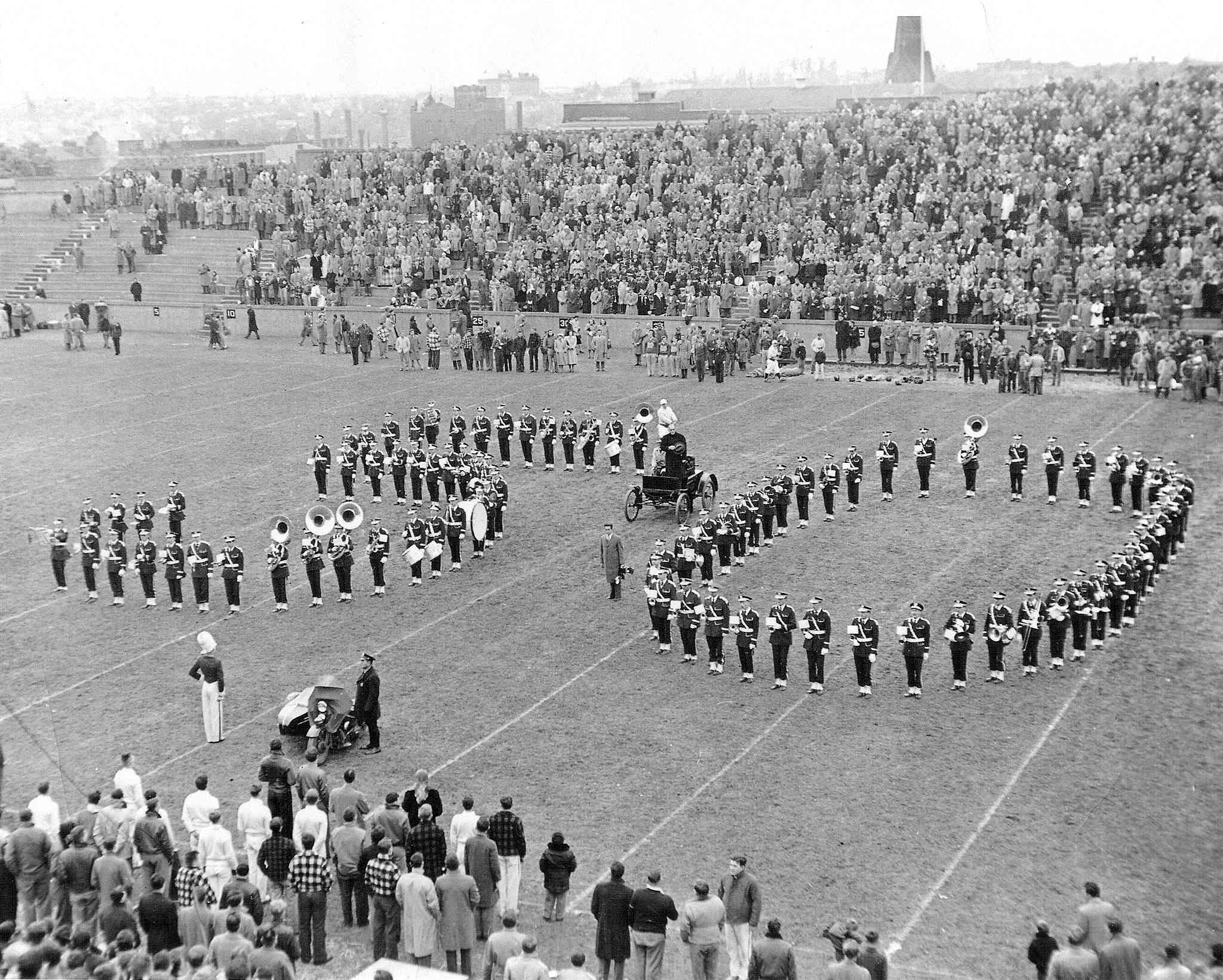The band forms a giant 50 on the football field with an old car driving down the middle
