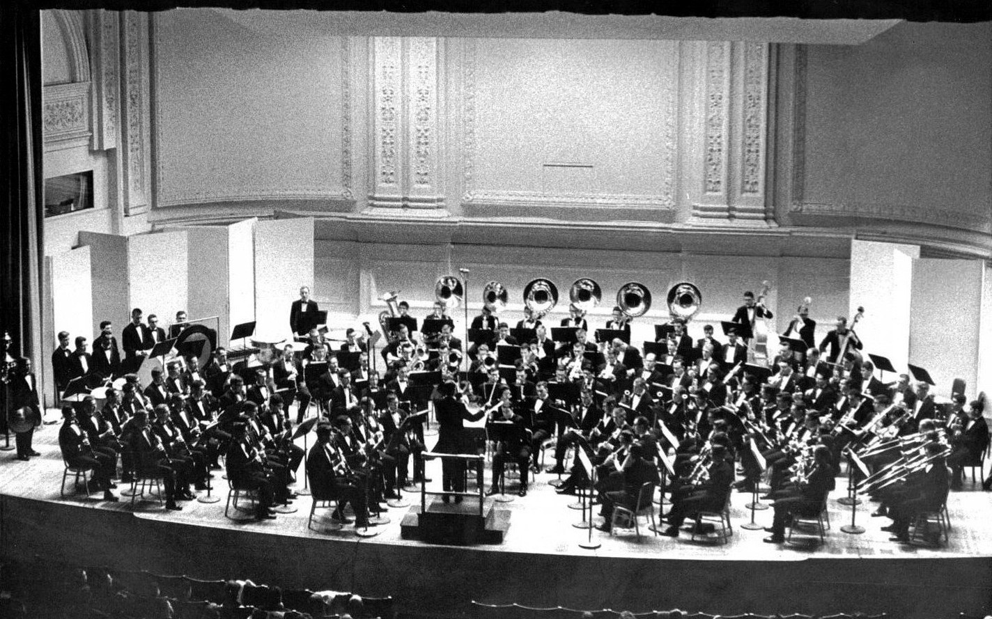 The band, dressed in tuxedos, rehearsing onstage with a conductor in front