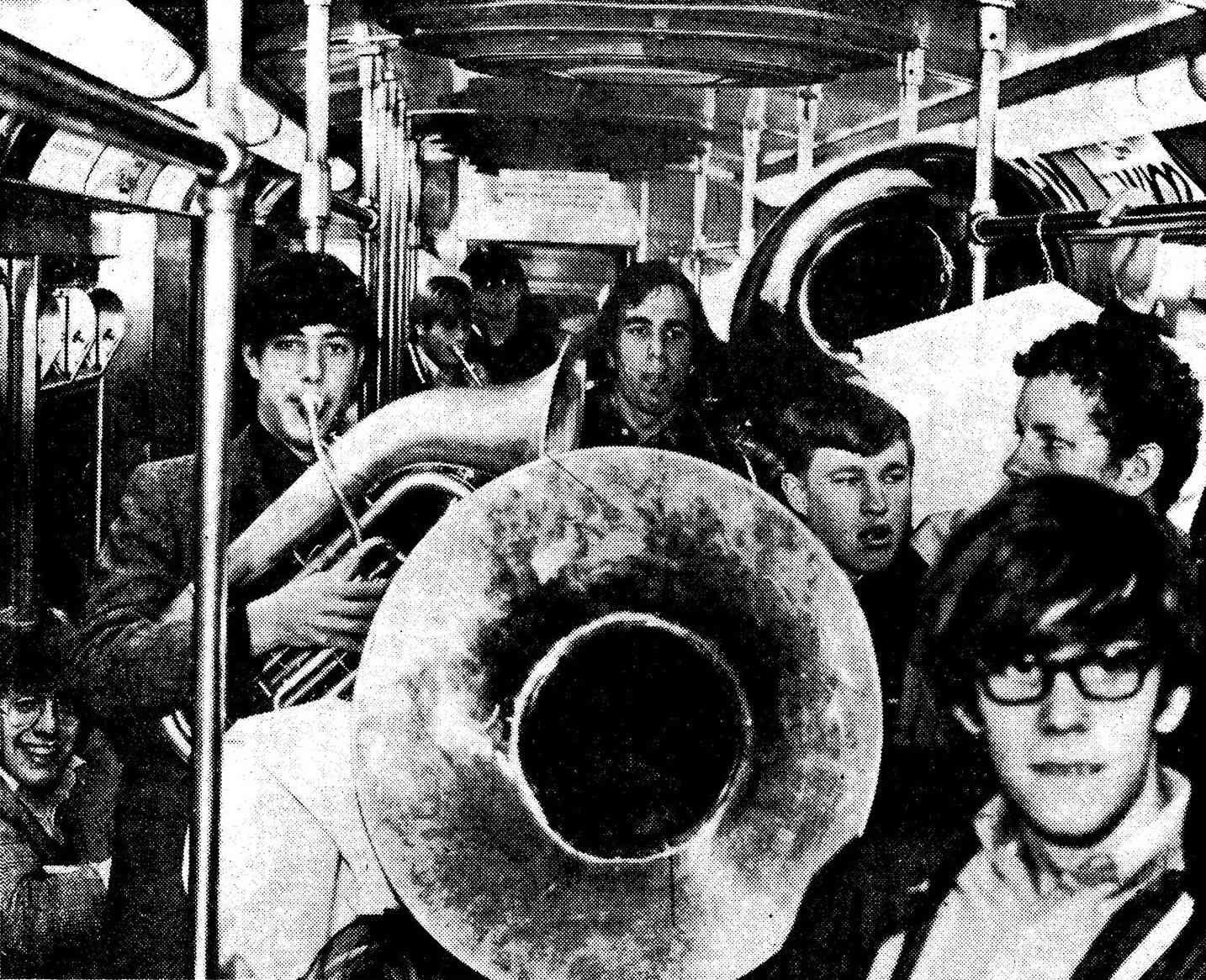 The band plays music on a subway while passengers watch and smile