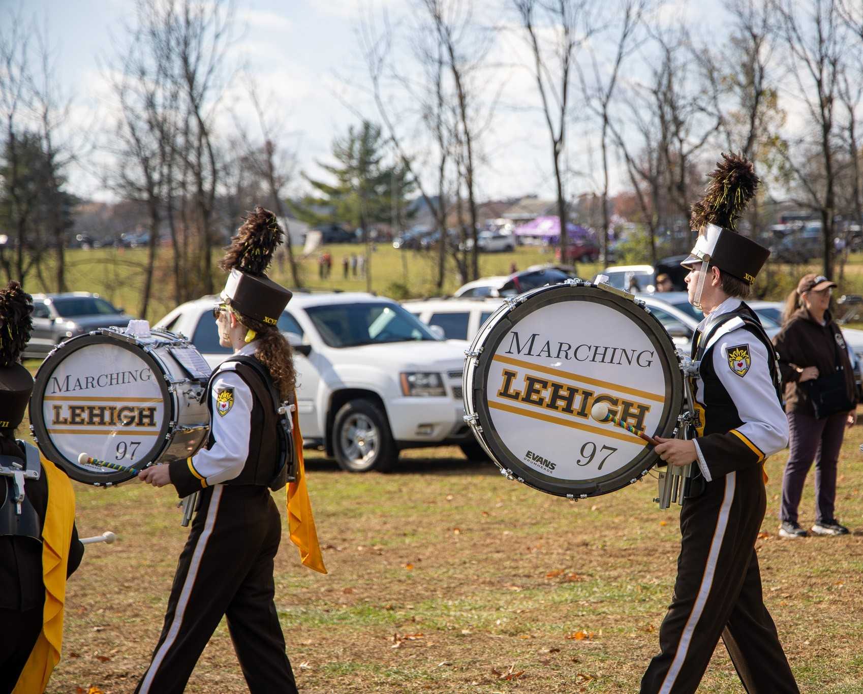 Bass drummers, their drums branded with the Marching 97 logo, playing while tailgating